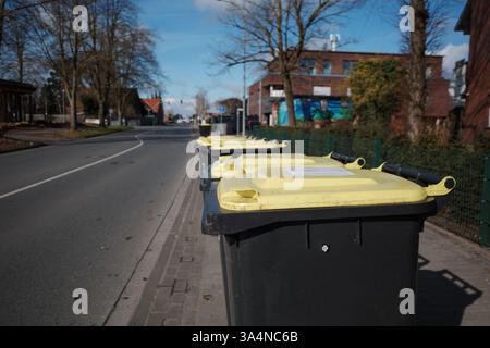 A row of black garbage bins with yellow lids lined up along a sidewalk in an urban residential area. Stock Photo