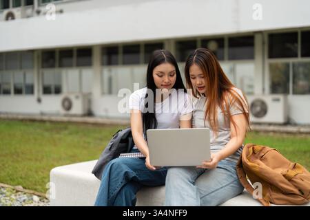 Students collaborating on a laptop, focused on their studies in a peaceful outdoor setting. Stock Photo