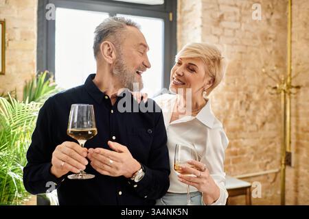 A middle-aged couple laughs and enjoys intimate moments over drinks in a cozy setting. Stock Photo