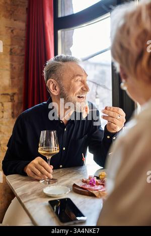 A joyful middle-aged couple enjoys their date, laughing over tasty food and drinks. Stock Photo