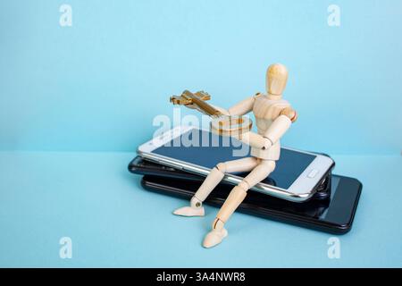 Wooden mannequin standing on smartphones stack and offering a golden key on blue background, internet security concept Stock Photo