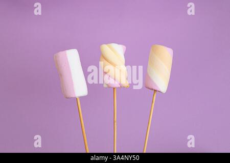 Three pastel colored marshmallows on wooden skewers, close up isolated on purple Stock Photo