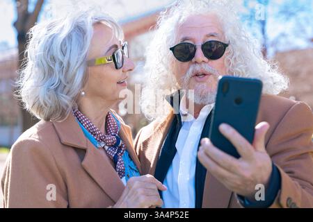 Senior couple using smartphone outdoors, enjoying technology and digital trends. Stock Photo