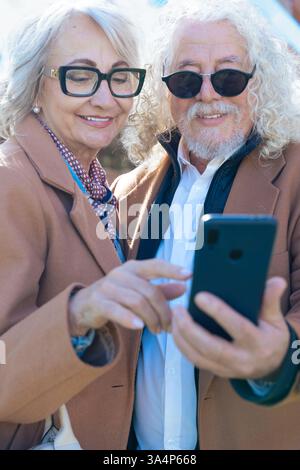 Senior couple using smartphone outdoors, enjoying technology and digital trends. Stock Photo