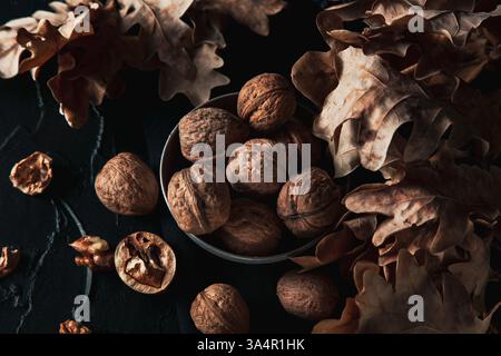 Several walnuts in an aluminum plate lie on a black background. dark autumnal composition Stock Photo