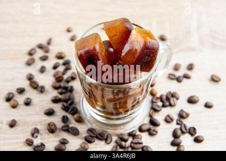 Side view of coffee ice cubes scattered on table, decorated with coffee beans. Studio shot. Concept of coffee ice cubes for making iced coffee. Stock Photo