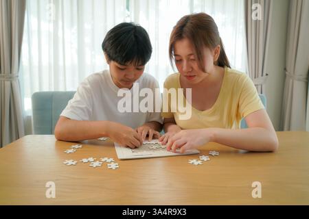 two asian friends working together on a puzzle at a wooden table, illustrating focus and teamwork. Stock Photo