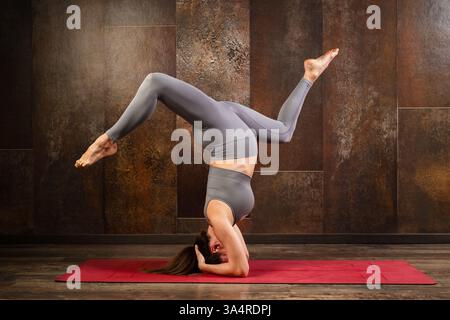 Pregnant woman doing yoga, showing balance and flexibility in a supported headstand pose Stock Photo