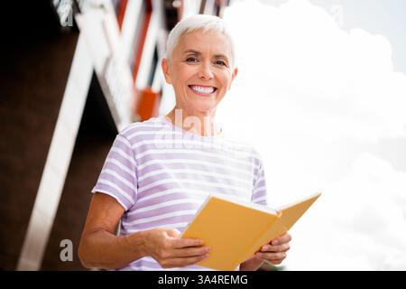 Elderly woman enjoying a book outdoors in the city, exuding charm and happiness Stock Photo