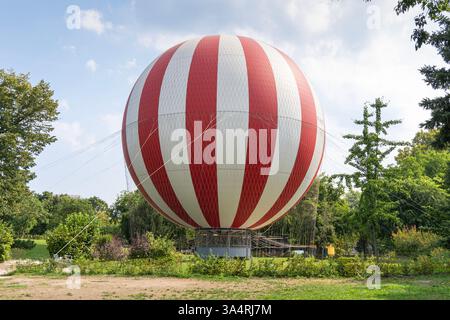 Large hot air balloon with red and white vertical stripes on the ground in a green field. Stock Photo