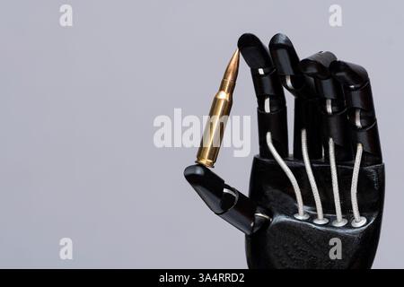 Robotic hand holds a bullet - Close-up of an artificial hand with black mechanical fingers holding a live round, symbolising technology, warfare and t Stock Photo