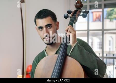Young musician playing the cello with bow and strings in his bedroom. Stock Photo