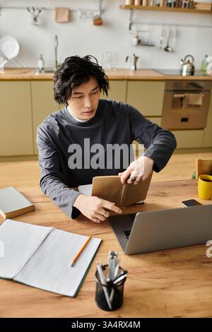 A handsome young man studies intently at home, using a laptop and surrounded by learning materials. Stock Photo