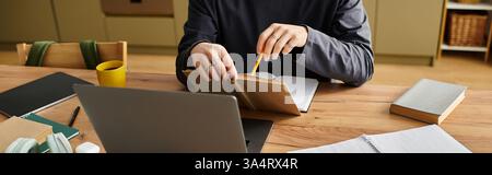 A young man focuses intently on his studies at home while using his laptop, banner Stock Photo