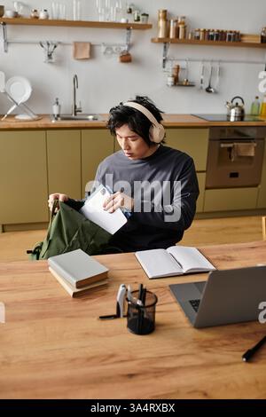 A young man engages in online learning at his home, focused on his studies and surrounded by books. Stock Photo