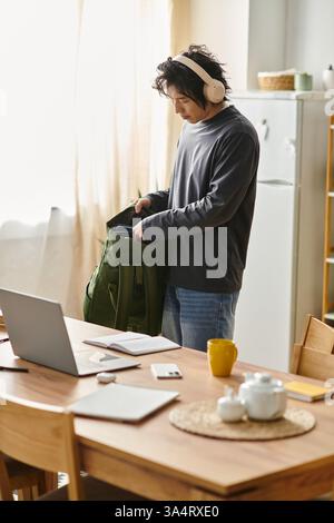 A focused young man organizes his study materials as he engages in online learning at home. Stock Photo