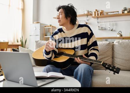 Handsome young man focuses on learning acoustic guitar while sitting comfortably at home. Stock Photo