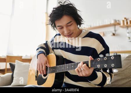 A young man practices playing his acoustic guitar, focused and immersed in his music lesson. Stock Photo