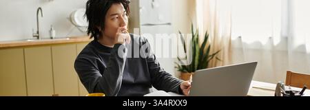 A handsome young asian student concentrates on his laptop while studying at home, banner Stock Photo