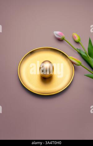 Glistening golden easter egg resting on an elegant golden plate, accompanied by three vibrant tulips, set against a rich brown background, symbolizing Stock Photo