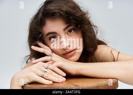 Charming young woman poses gracefully with hands on a wooden surface, exuding confidence. Stock Photo
