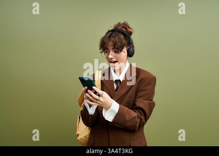 A young woman in a unique brown suit shows excitement while using her smartphone. Stock Photo