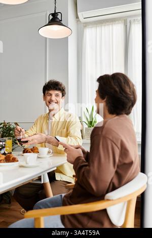 Two men enjoy breakfast together, exchanging smiles and laughter in their chic living space. Stock Photo