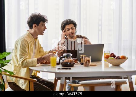 Two good-looking men enjoy breakfast and engage in conversation at their modern dining table. Stock Photo