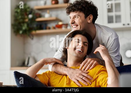 Two smiling gay couple embraces in a stylish apartment, sharing a tender and happy moment together. Stock Photo