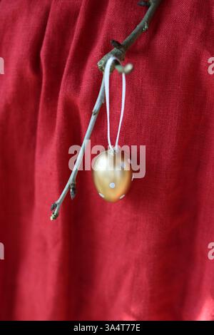 Golden egg hanging on a tree branch on a red fabric background. Stock Photo