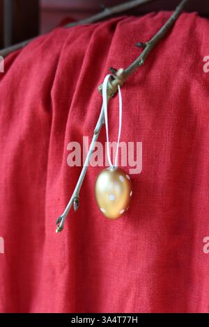 Golden egg hanging on a tree branch on a red fabric background. Stock Photo