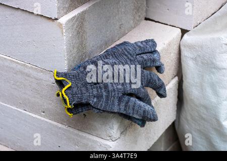 A pair of warm gloves gently resting atop a large, uneven pile of bricks that are stacked haphazardly together in a construction site, Stock Photo