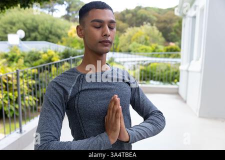 Young man practicing yoga on balcony, meditating with hands in prayer position, copy space Stock Photo