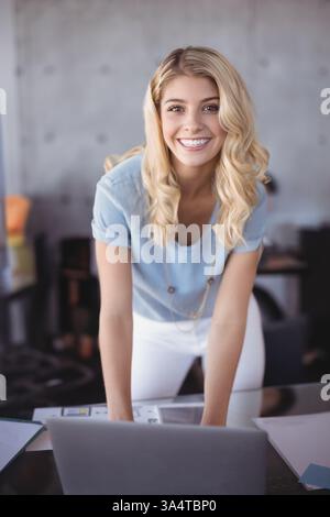 Smiling woman leaning over desk using laptop in modern office environment Stock Photo