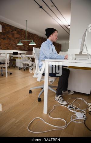 Young professional in beanie working on computer at modern office desk, copy space Stock Photo