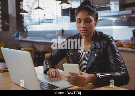 Young woman using smartphone and laptop in trendy cafe, concentrating on work Stock Photo