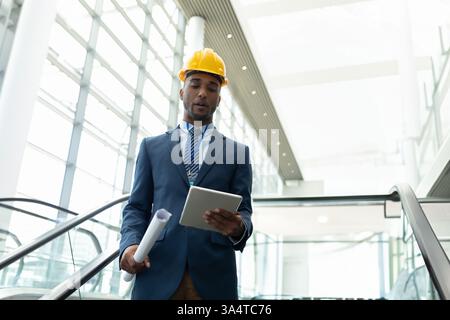 Engineer in suit and hard hat reviewing plans on tablet in modern building, copy space Stock Photo