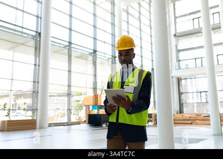 Engineer in safety vest and hard hat using tablet in modern building, copy space Stock Photo