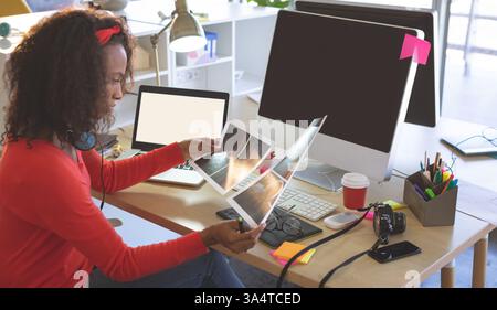 Creative professional reviewing design prints at modern office desk with technology, copy space Stock Photo