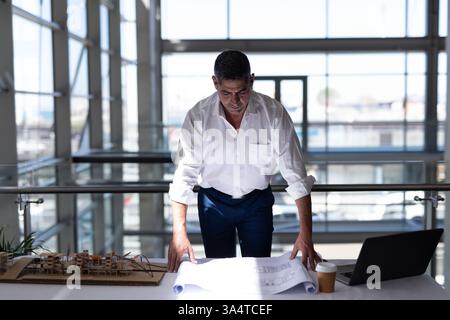 Architect reviewing blueprints at office desk with model and laptop Stock Photo