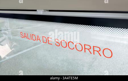 Close-up of the words "Salida de Socorro" (Social Exit) on a red Spanish emergency exit sign in a window inside a public transportation vehicle. Stock Photo