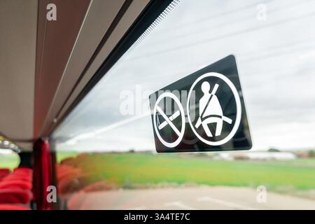 No smoking warning next to a seat belt sign on a bus window. Stock Photo
