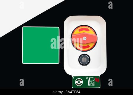 An emergency exit sign with an opening switch on a black and white background next to a green sticker with copy space. Stock Photo