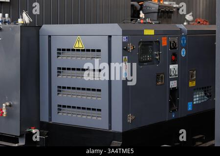 An industrial generator hums quietly in the workshop, providing reliable power. Bright fluorescent lights illuminate the space, showcasing tools and e Stock Photo