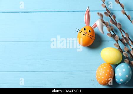 Bright Easter eggs and willow branches on light blue wooden table, top view. Orange one with bunny ears and face Stock Photo