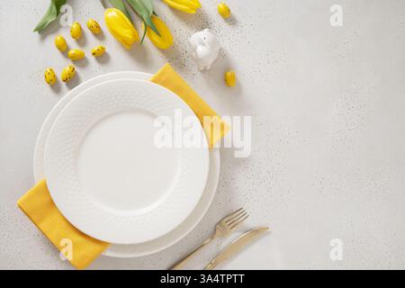Easter table setting with spring, yellow tulips, white plates, bunny, eggs on white background. Festive place setting. Holidays background. Copy space Stock Photo