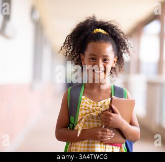 Smiling girl holding book in school hallway, ready for class Stock Photo