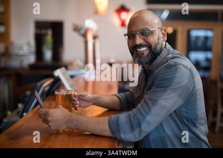 Smiling man enjoying beer and using smartphone at cozy bar counter, copy space Stock Photo