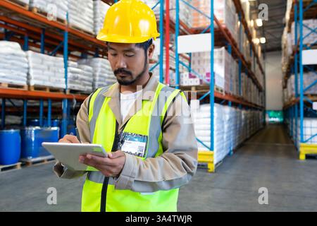 Warehouse worker in safety vest using tablet for inventory management, copy space Stock Photo