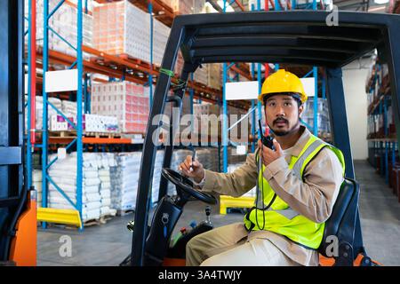 Warehouse worker in safety gear operating forklift and communicating via radio, copy space Stock Photo